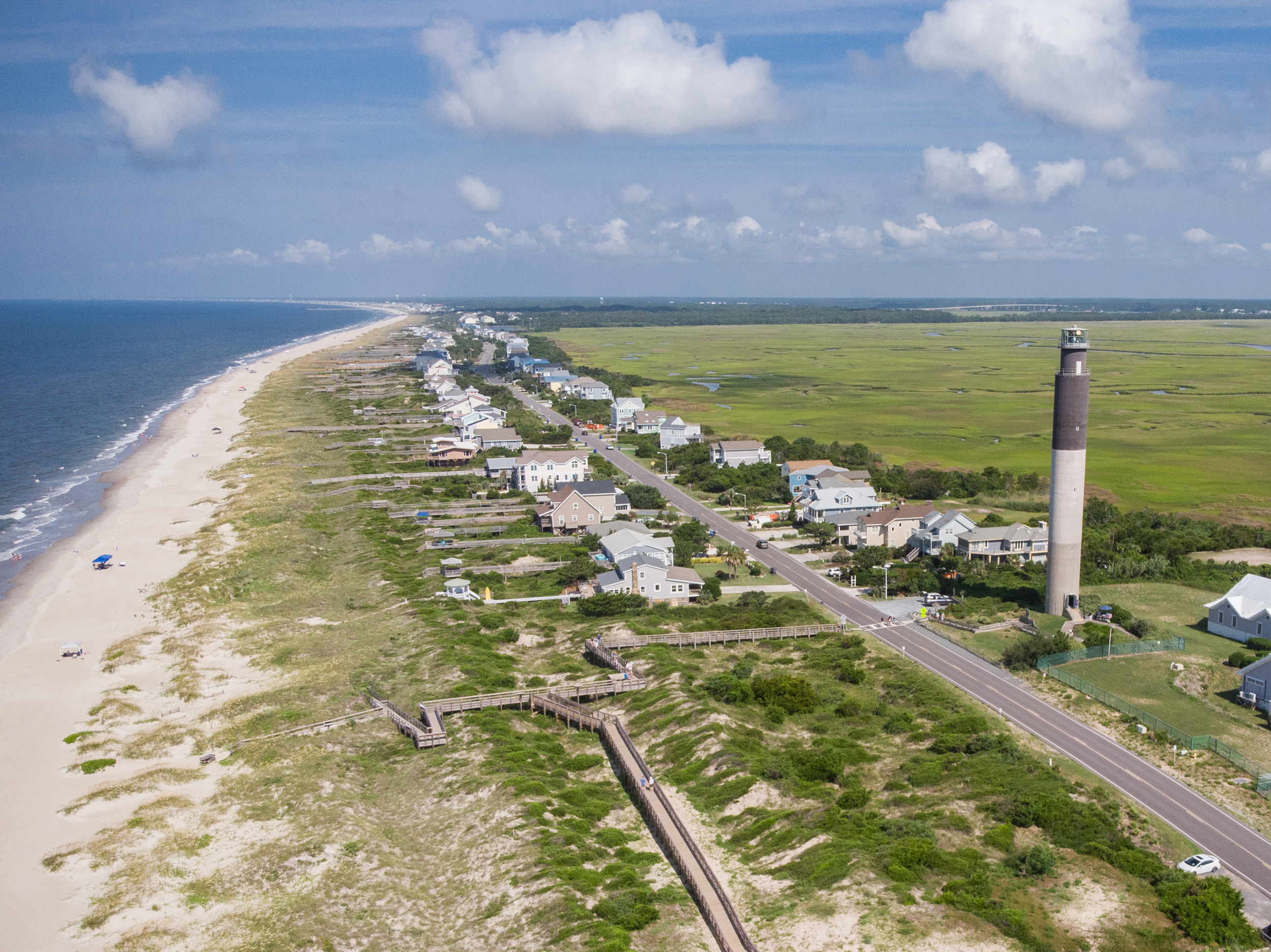 Brunswick County NC real estate – aerial view of Oak Island featuring coastal homes, the Oak Island Lighthouse, and the Atlantic Ocean.