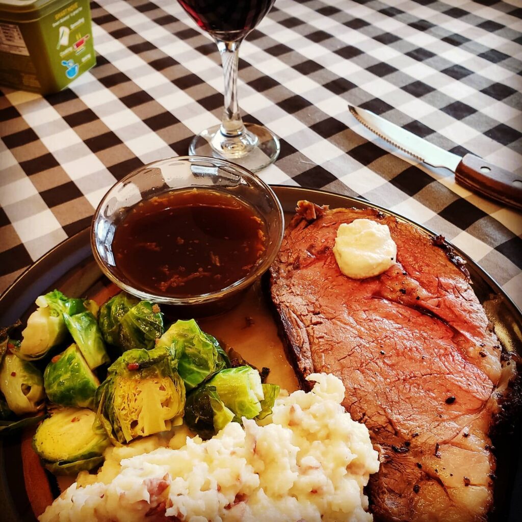 Sold on Flavor prime rib dinner with mashed potatoes, roasted Brussels sprouts, au jus, and a glass of red wine.